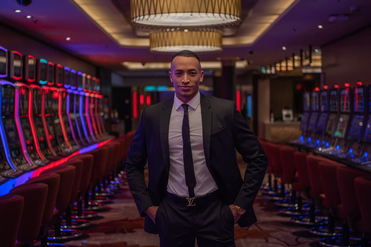 get-in-touch Businessman standing confidently in a luxurious casino with rows of gaming machines.